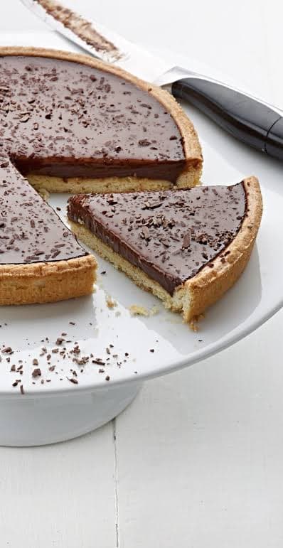 A chocolate ganache tart on a cake stand with one slice cut and lifted