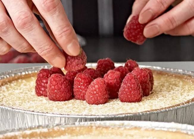 An operator hand-placing fresh raspberries onto a dessert base in a foil tray