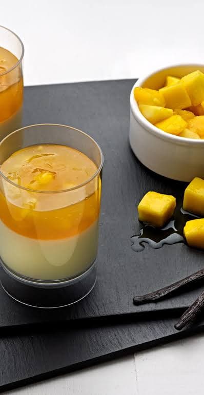 Layered mango and vanilla dessert pots on slate with fresh mango and vanilla pods