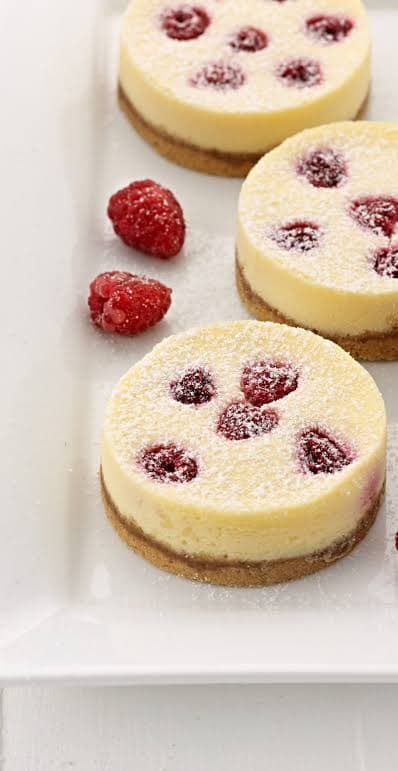 Raspberry cheesecakes dusted with icing sugar on a white serving plate